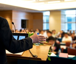 Business man is making a speech in front of a big audience at a conference hall.