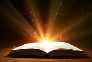 Old open book with magic light and falling stars on wooden table