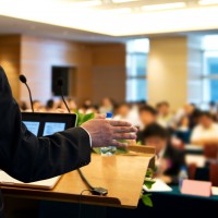 Business man is making a speech in front of a big audience at a conference hall.